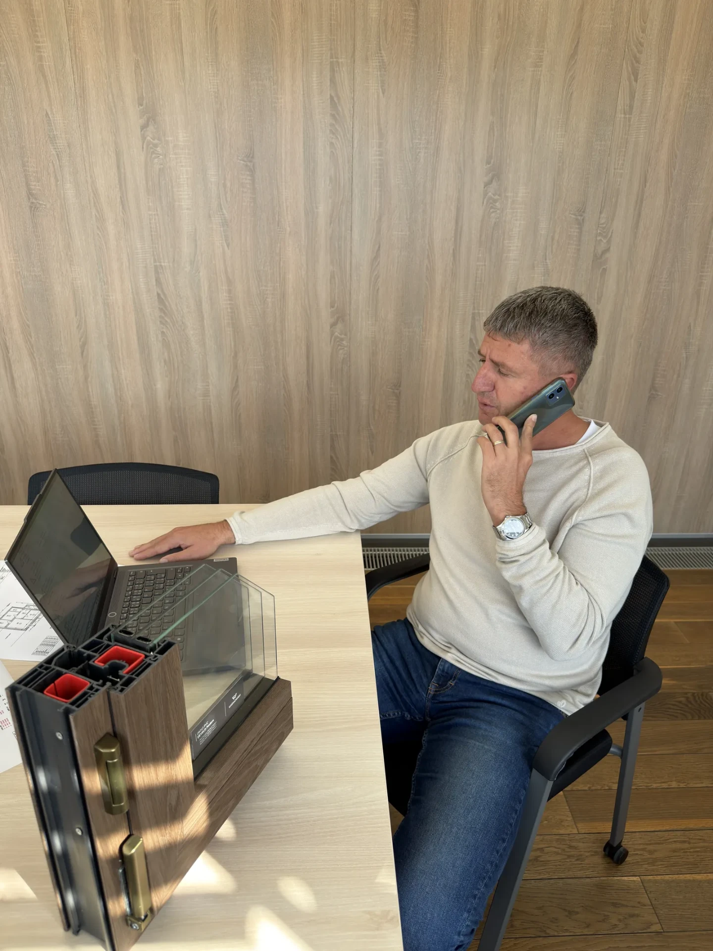 Poradce NZÚ Renovace telefonuje, na stole vzorek okna
